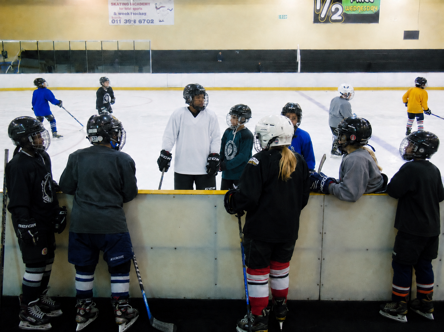 Young ice hockey players gathered at the boards during beginner practice.